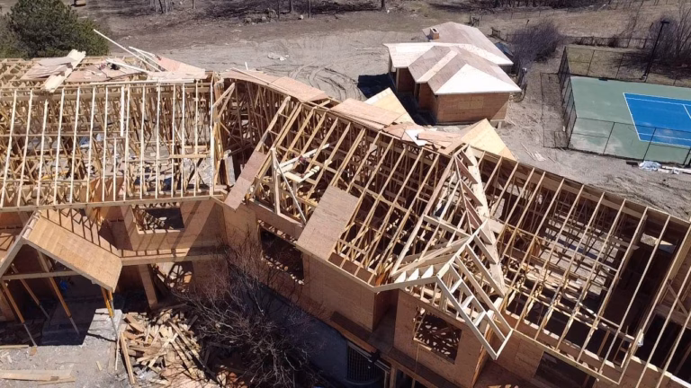 Aerial view of a house under construction, showcasing exposed wooden framing and a nearby tennis court.