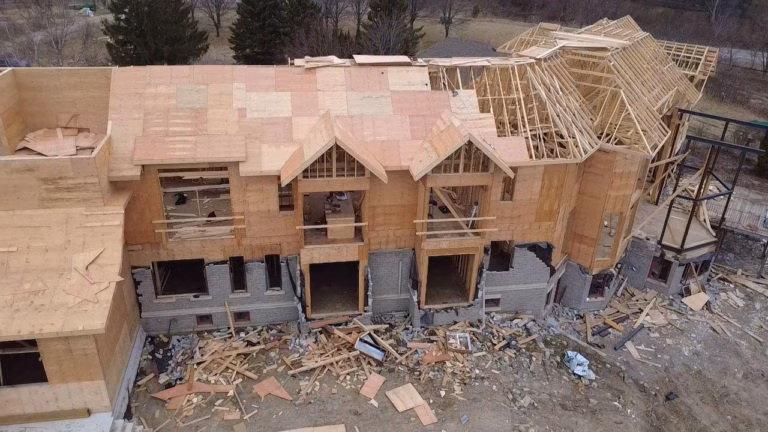 Aerial view of a house under construction, featuring an unfinished wooden frame, exposed walls, and debris scattered around the site.